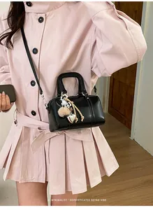 Detail of black glossy pillow bag with heart charm, held by model in pink dress
