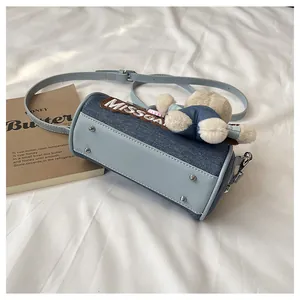 Detail of blue denim Boston bag with plush bear charm and metallic bottom studs