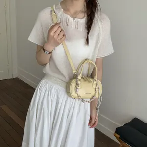 Minimalist pale yellow cylindrical shoulder bag with crossbody strap and checkerboard chain
