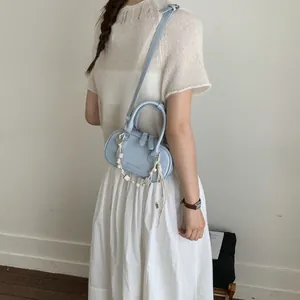 Light blue minimalist leather handbag with beaded pendant shown in a stylish studio shot