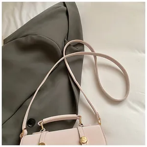 Detailed view of beige square handbag featuring a gold buckle and elegant stitching