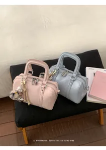 Close-up of pink and blue mini Boston bags with plush ball charms and top zipper detail
