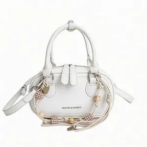 Minimalist white leather oval crossbody bag with woven pendant and adjustable shoulder strap