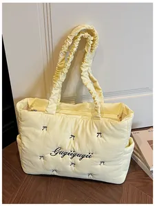 Detail of light yellow quilted tote bag featuring black bow embroidery and ruched straps
