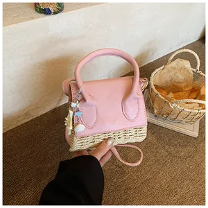 Pink straw weave mini handbag with shell charms held in a warm lifestyle setting