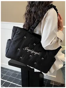 Detail of black quilted nylon tote bag featuring white bow embroidery and pleated strap