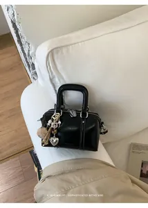 Detail of black leather Boston bag with decorative heart charm and plush ball accessory