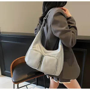 Model wearing a grey-blue hobo bag with front zip pockets and a minimalist crescent shape