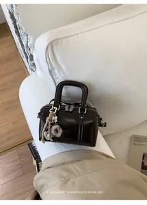 Detail of a dark brown glossy pillow bag with silver zippers and heart charm accessory