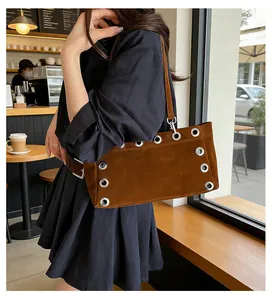 Detailed view of brown suede baguette bag with large silver grommets and metal eyelets