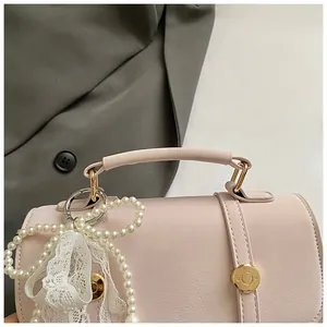 Detail of pink cylindrical handbag with pearl chain and lace bow decoration