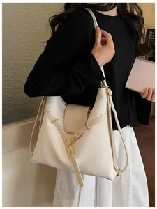 Detail van minimalistische crème hobo tas met kruislings lederen riempjes en gespen