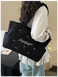 Detail view of black quilted nylon tote with white embroidered bows and soft pleated strap