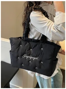 Detail of black quilted nylon tote bag with white bow embroidery and ruffled handles