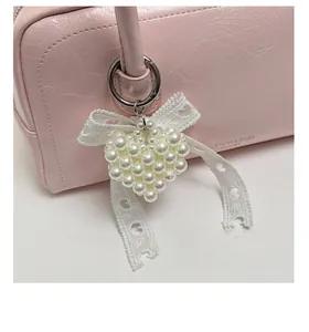 Détail d'un pendentif cœur en perles blanches avec nœud en dentelle sur sac rose