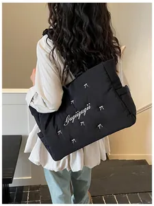 Detail of black quilted nylon tote featuring white bow accents and embroidered logo