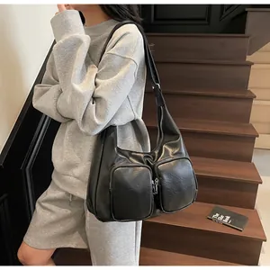 Detail view of a black matte leather hobo bag with front zip pockets on a model