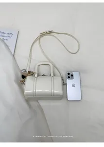 Detail of a creamy white Boston bag next to an iPhone for size reference on white fabric