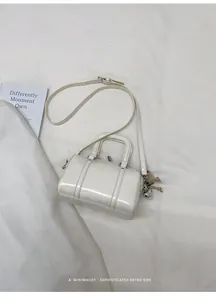 Close-up of a white glossy Boston bag with heart pendant and adjustable shoulder strap