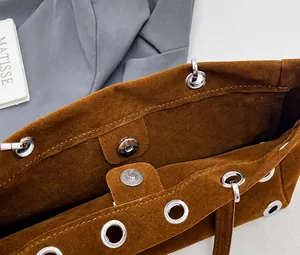 Detail view of the magnetic clasp and metal eyelets on this brown suede baguette bag