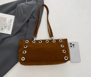Close-up of brown suede baguette bag featuring large silver metal grommets and shoulder strap