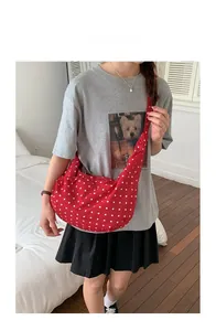 Close-up of red and white polka dot canvas shoulder bag shown on a model