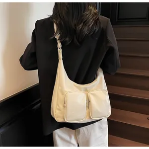 Detail of a creamy white crescent bag featuring two front zipper pockets and silver hardware