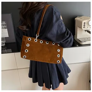 Detail of brown suede baguette bag featuring silver metal eyelets and a slim shoulder strap
