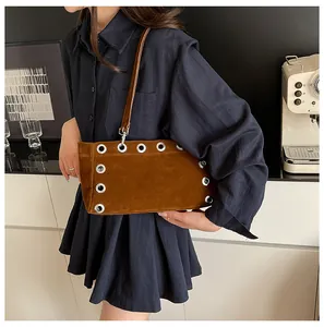 Detail of a brown matte baguette bag featuring silver grommets and slender shoulder strap