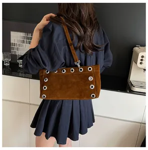 Detail of brown suede baguette bag featuring silver metal eyelets and shoulder strap
