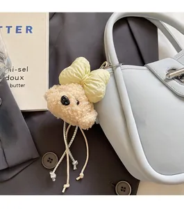 Close-up of cute beige teddy bear plush charm with bow attached to a blue leather bucket bag