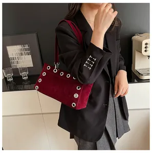 Detail of burgundy velvet baguette bag featuring silver metal grommets and suede texture