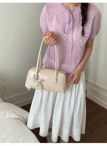 Détail d'un sac à main crème en cuir avec charme cœur perlé et nœud en dentelle