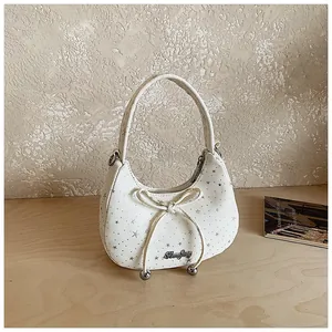 Detail van witte canvas hobo tas met zilveren sterren, strik en metalen voetjes
