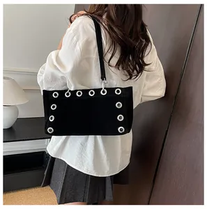 Detail of black suede shoulder bag with large silver metal grommets and slim strap