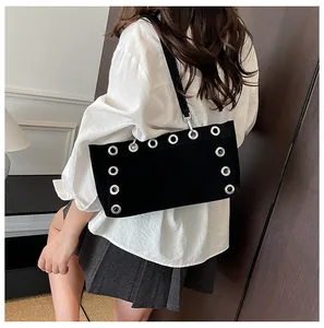 Detail of black matte baguette bag with silver eyelets worn on model shoulder