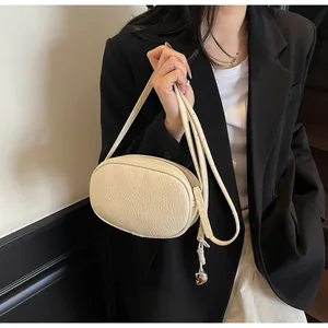 Close-up of beige oval shoulder bag with pleated texture and silver heart pendant detail
