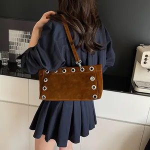Brown matte suede baguette bag with metal eyelets worn over the shoulder by a model