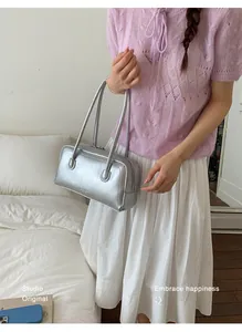 Sac à bandoulière argenté brillant porté par un mannequin en pull violet et jupe