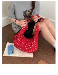 Lifestyle view of a large red canvas hobo bag with white polka dots worn by a model