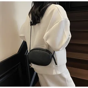 Close-up of black lychee grain leather crossbody bag styled with a white sweatshirt