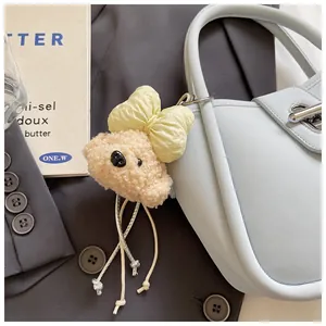 Close-up of a plush beige dog charm with a yellow bow attached to a blue leather bag