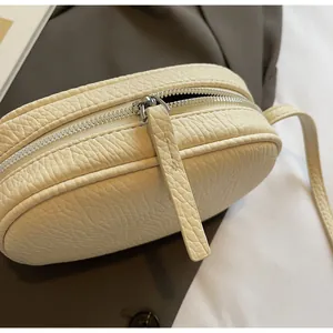 Detail of minimalist cream leather pillow bag showing litchi texture and silver zipper