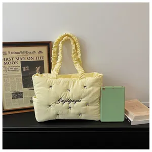 Detail of yellow quilted tote bag with bow embroidery and side pocket next to a tablet