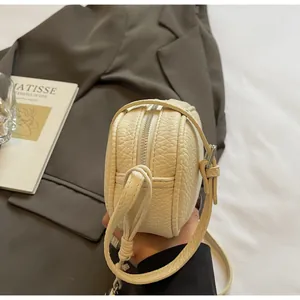 Detailed view of off-white lychee leather bag with silver zipper and adjustable strap