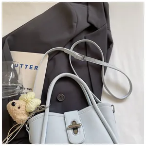 Detail of light blue bucket bag with silver twist lock, long strap and bear charm