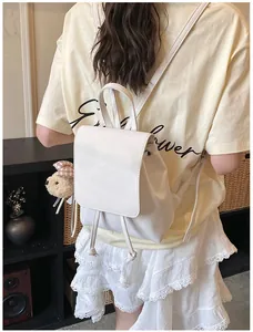 Detailed back view of a minimalist white mini backpack with plush bear charm on a model