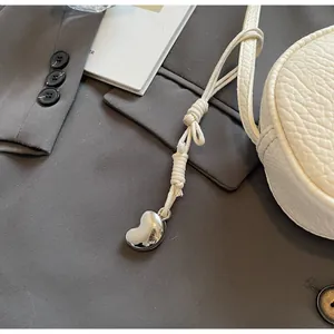 Detail of white lychee leather pillow bag with knotted strap and silver heart pendant