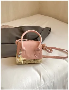 Close-up of pink leather and woven straw bag with starfish charm on white fabric