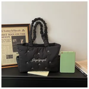 Detail of quilted nylon tote bag with bow embroidery and side pocket for tablet